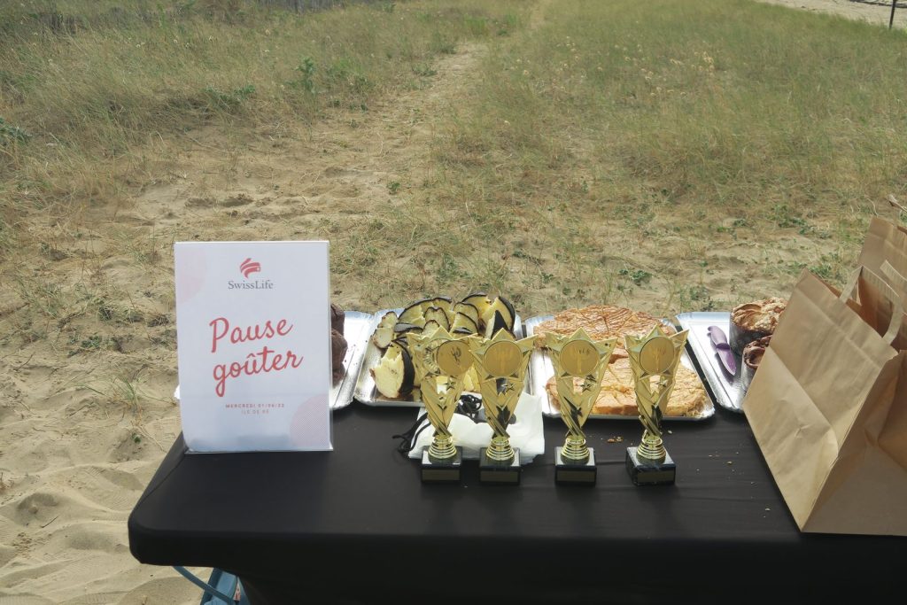 Table de la pause goûter sur la plage après les Olympiades, avec gâteaux, trophées dorés et chevalet « Pause goûter » aux couleurs de Swiss Life