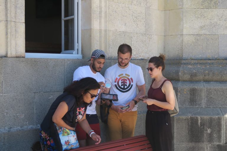 Équipe du séminaire Swiss Life penchée sur une tablette et une loupe, au pied d’un mur en pierre, pendant l’escape game autour du phare des Baleines, sur l’île de Ré.