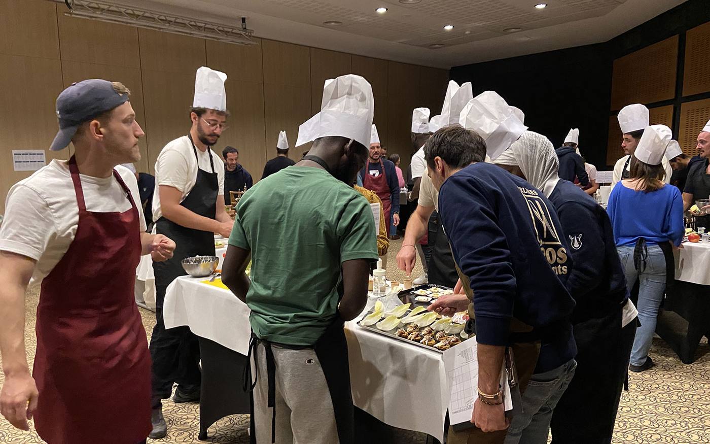 Participants du séminaire incentive LIBON coiffés de toques blanches autour des plans de travail d'un cooking challenge, organisé par Weevup au Pays basque