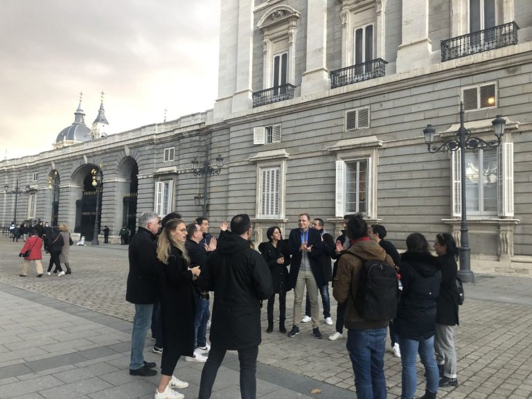 Les participants du séminaire de Norman K réunis en cercle devant le Palais royal de Madrid pendant le team building, la cathédrale de l’Almudena au fond