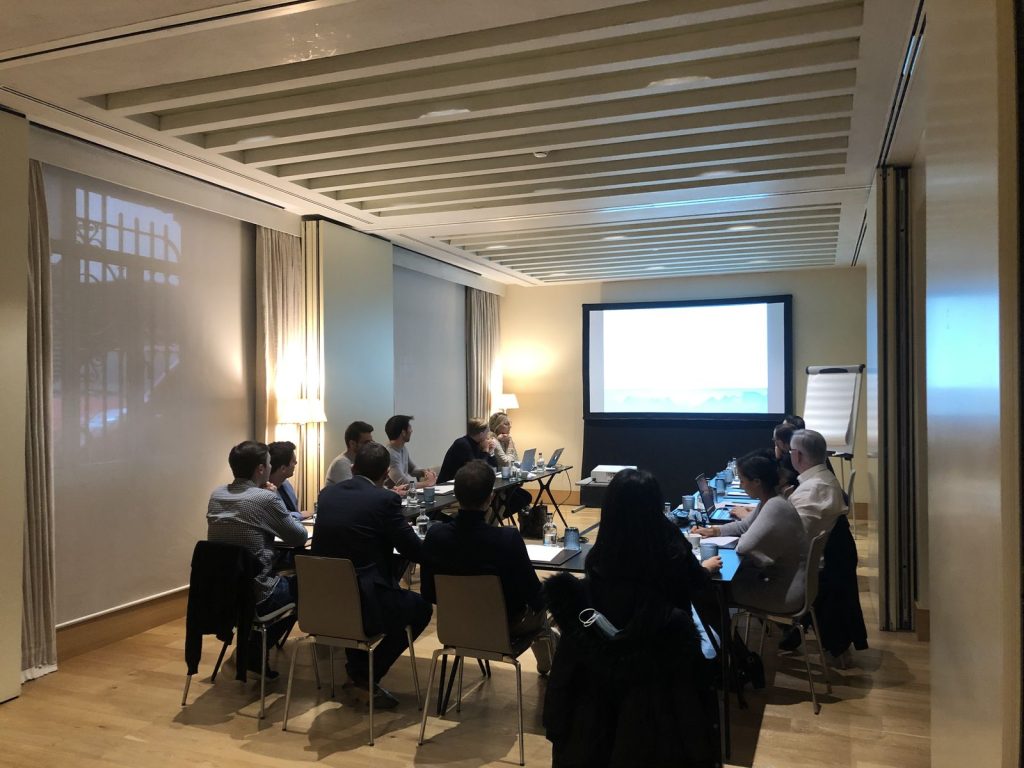 Réunion de travail de Norman K dans une salle de l’Hôtel Urso à Madrid, les participants attablés face à un écran
