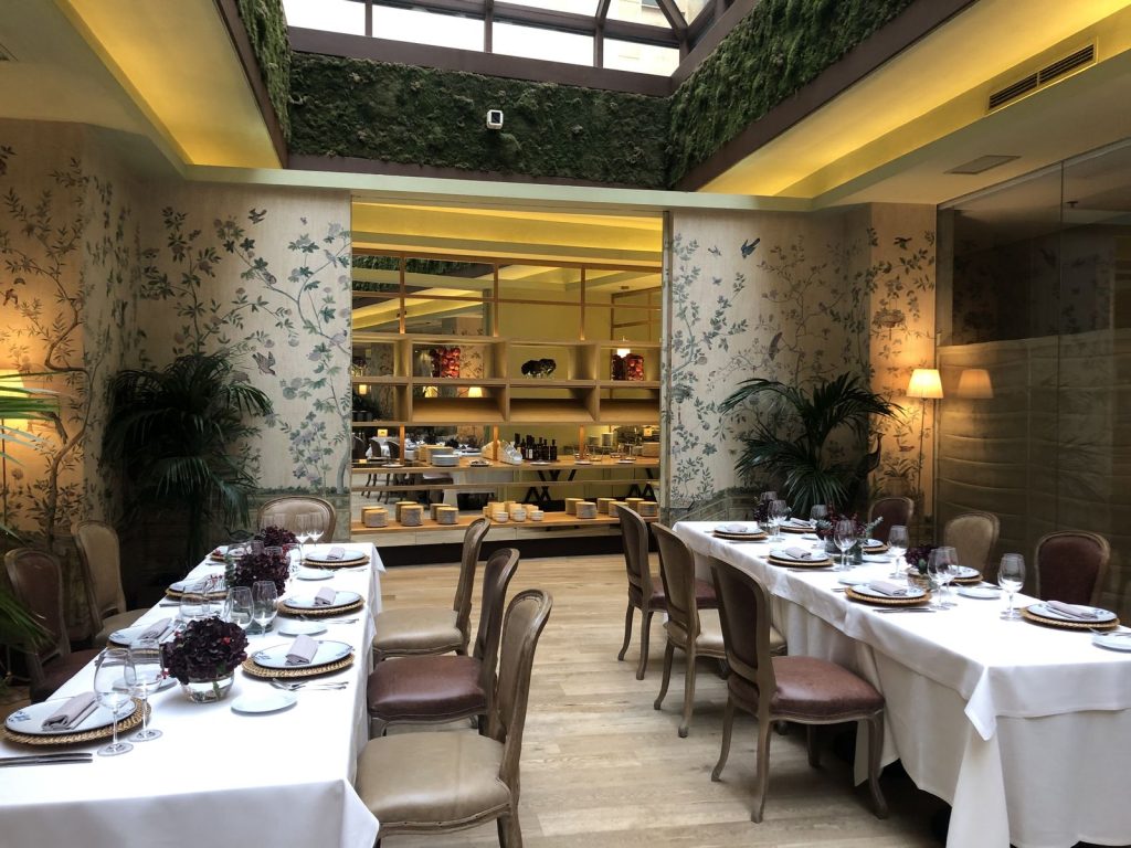 Tables dressées sous la verrière d’une salle de l’Hôtel Urso, buffet en arrière-plan, pour le déjeuner du séminaire de Norman K