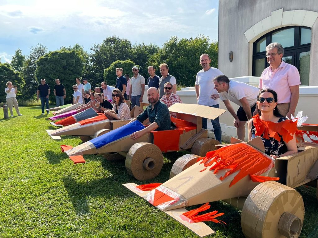 Sept Formules 1 en carton alignées sur la pelouse du Radisson Paris Marne-la-Vallée, des collaborateurs de Partecis assis à bord, pendant le team building du séminaire.