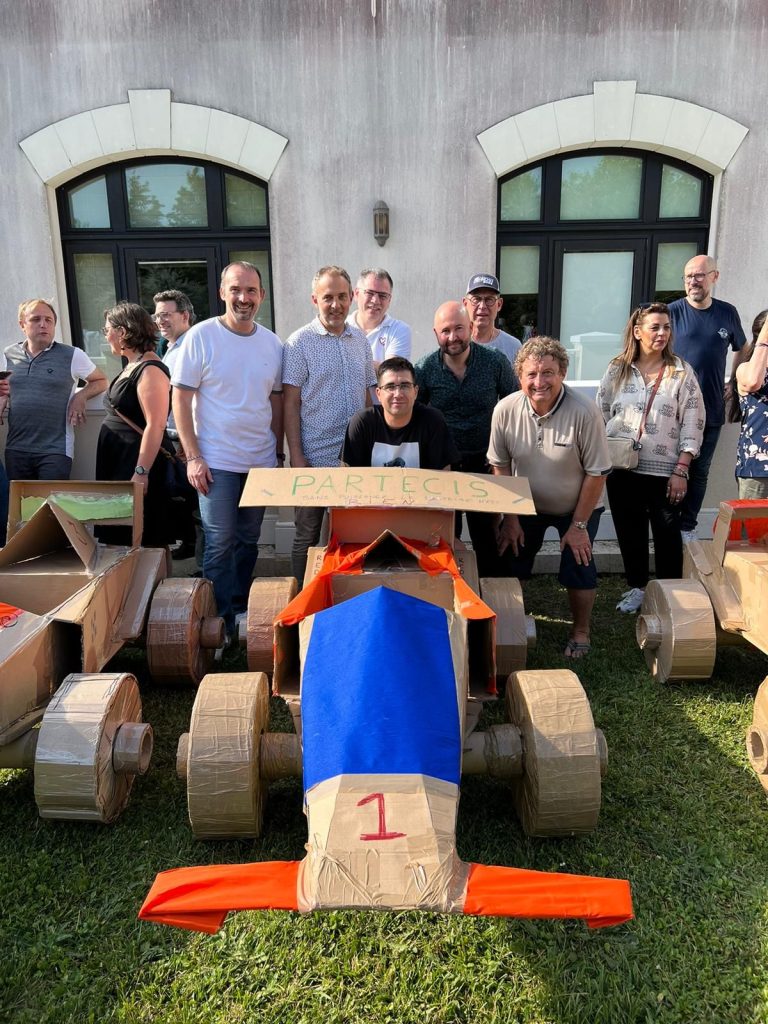 Une équipe de Partecis derrière sa Formule 1 en carton numéro 1, aileron marqué PARTECIS, devant la façade de son hôtel de Marne-la-Vallée