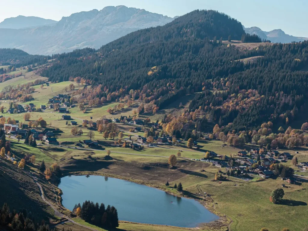 Un lac au creux de la vallée de La Clusaz, entre prairies et forêts d’automne, dans le massif des Aravis