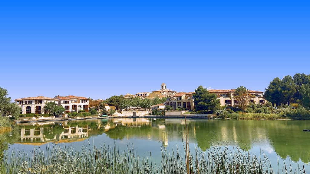 Bâtiments aux façades ocre et toits de tuiles du village de Pont Royal en Provence, reflétés dans un lac bordé de roseaux, lieu d'un séminaire de 162 personnes organisé par Weevup