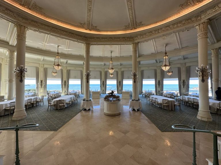 Salle de restaurant en rotonde aux colonnes blanches et lustres en cristal, tables nappées face aux baies vitrées ouvertes sur l’océan, pendant le séminaire résidentiel Husqvarna organisé par Weevup à Biarritz