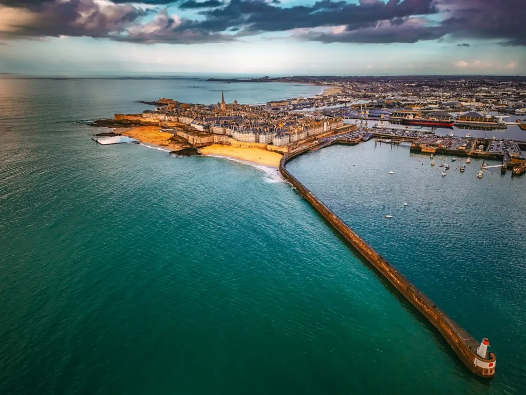Vue aérienne de Saint-Malo intra-muros, de ses remparts et de sa plage, avec une longue jetée et son phare au premier plan