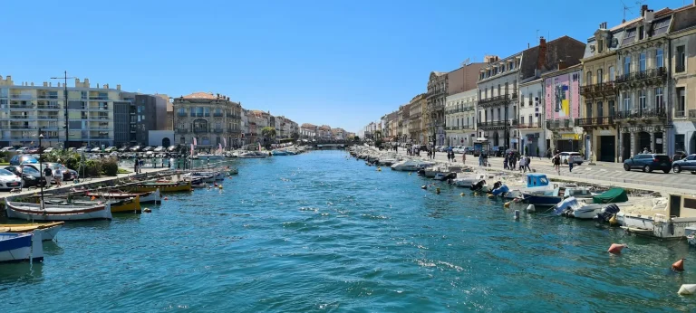 Bateaux amarrés le long d’un canal de Sète, bordé de quais et de façades colorées, sous un ciel bleu