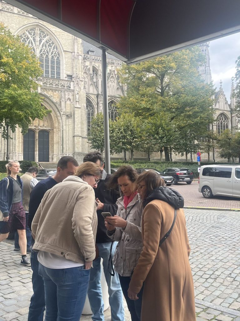 Une équipe du séminaire Swiss Life regroupée autour d’un smartphone au départ du rallye, devant l’hôtel, face à l’église Notre-Dame du Sablon à Bruxelles