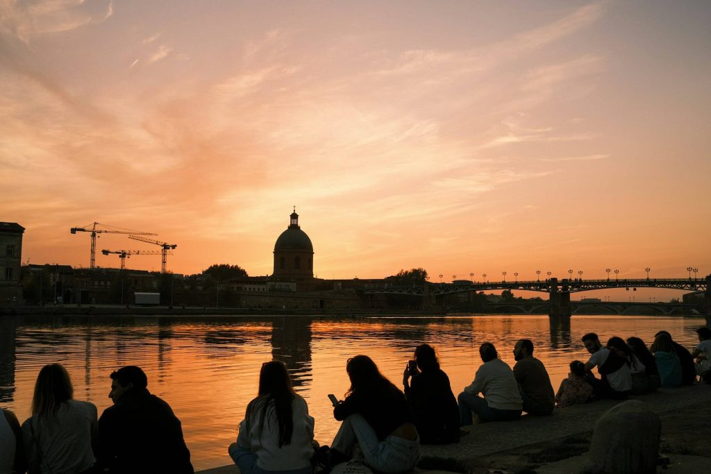 Promeneurs assis sur les quais de la Garonne au coucher du soleil, face au dôme de la Grave, à Toulouse