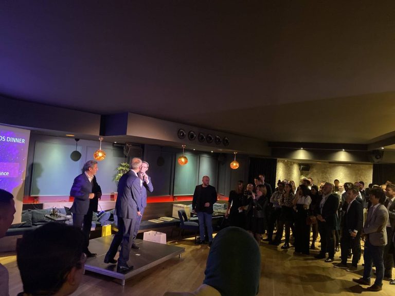 Intervenants en costume sur une estrade, l’un d’eux au micro, face aux invités debout lors d’une soirée Scalian organisée par Weevup