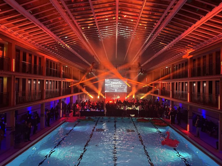 Scalian awards dinner at the Molitor: glass roof and galleries lit in orange, guests on the covered part of the pool facing the Awards Dinner LED screen, inflatable flamingos on the water