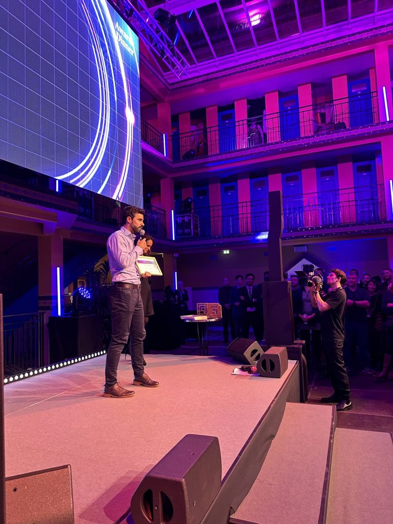 Remise des prix de la soirée awards Scalian au Molitor : un intervenant au micro sur scène, diplôme encadré en main, trophées en bois posés sur un guéridon