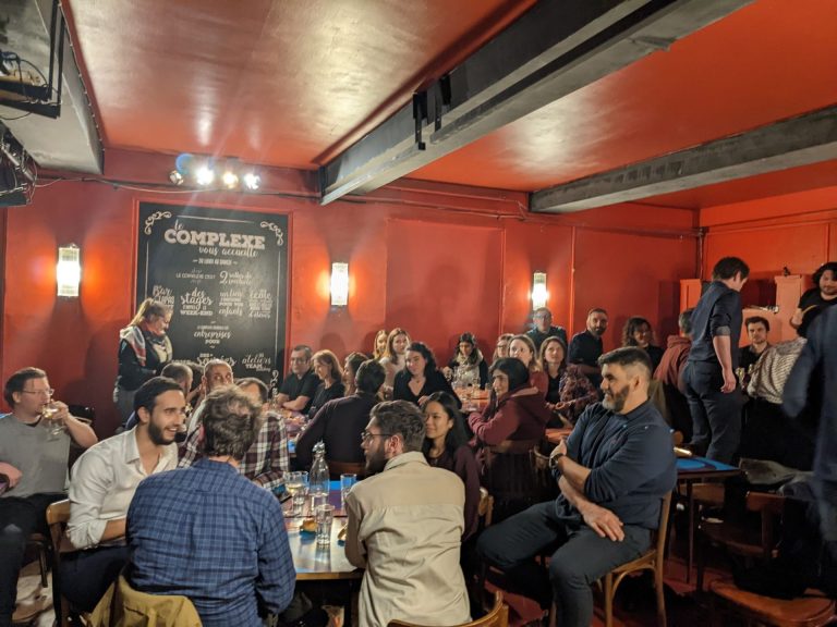Salle du Complexe du Rire à Lyon remplie d'invités attablés, murs rouges et tableau « Le Complexe vous accueille », pendant la soirée d'entreprise de Tyredating.