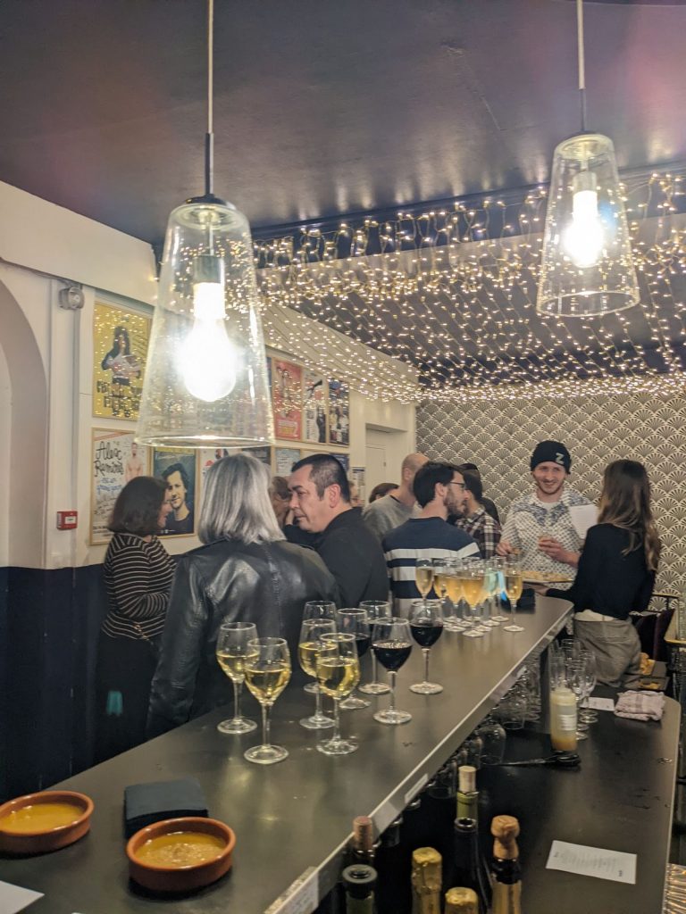 Invités réunis au bar du Complexe du Rire sous une guirlande lumineuse, flûtes de champagne et verres de vin blanc et rouge servis, soirée Tyredating à Lyon