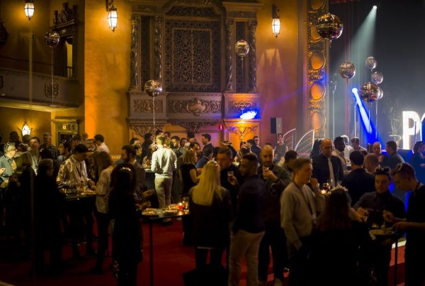 Cocktail de la convention du Groupe Positive au Plaza Hotel de Bruxelles, organisée par Weevup : invités debout autour de mange-debout dans une salle de spectacle aux décors dorés, sous des ballons argentés et des projecteurs bleus