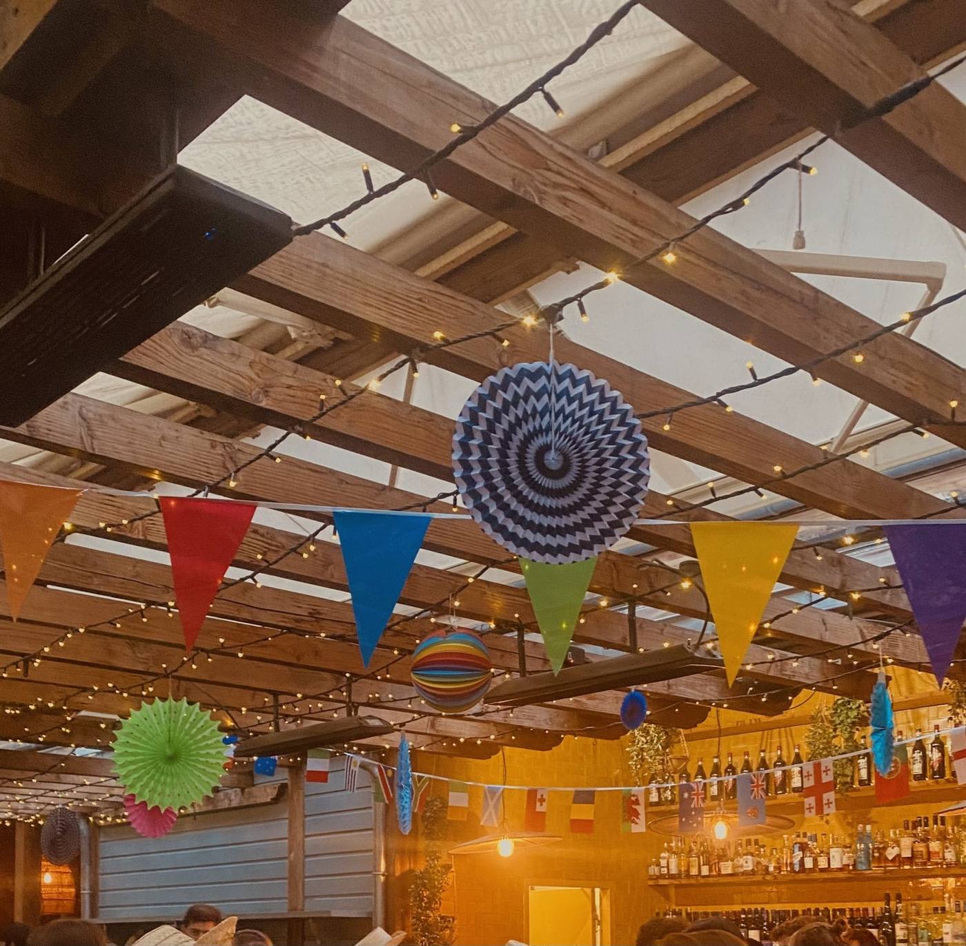 Plafond à poutres de la Brasserie Auteuil décoré de fanions colorés, de rosaces en papier et de guirlandes lumineuses pour la soirée de rentrée de Coty organisée par Weevup