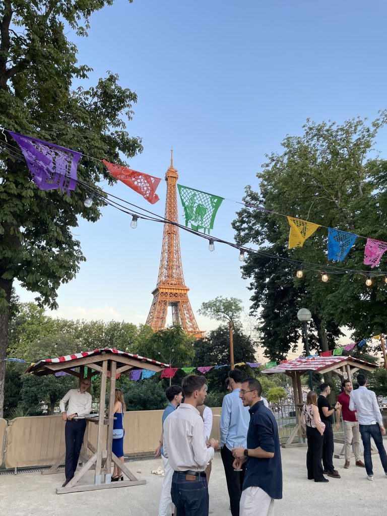 Summer Party KPMG à l’Aquarium de Paris : la tour Eiffel au-dessus de la terrasse, fanions en papier découpé, guirlandes et participants autour des mange-debout en bois