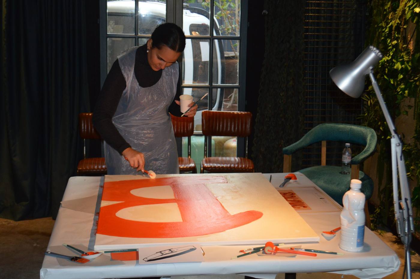 Participante en tablier peignant de grandes formes orange sur une toile posée à plat, pendant le team building créatif Hermès organisé par Weevup au Kube Hôtel