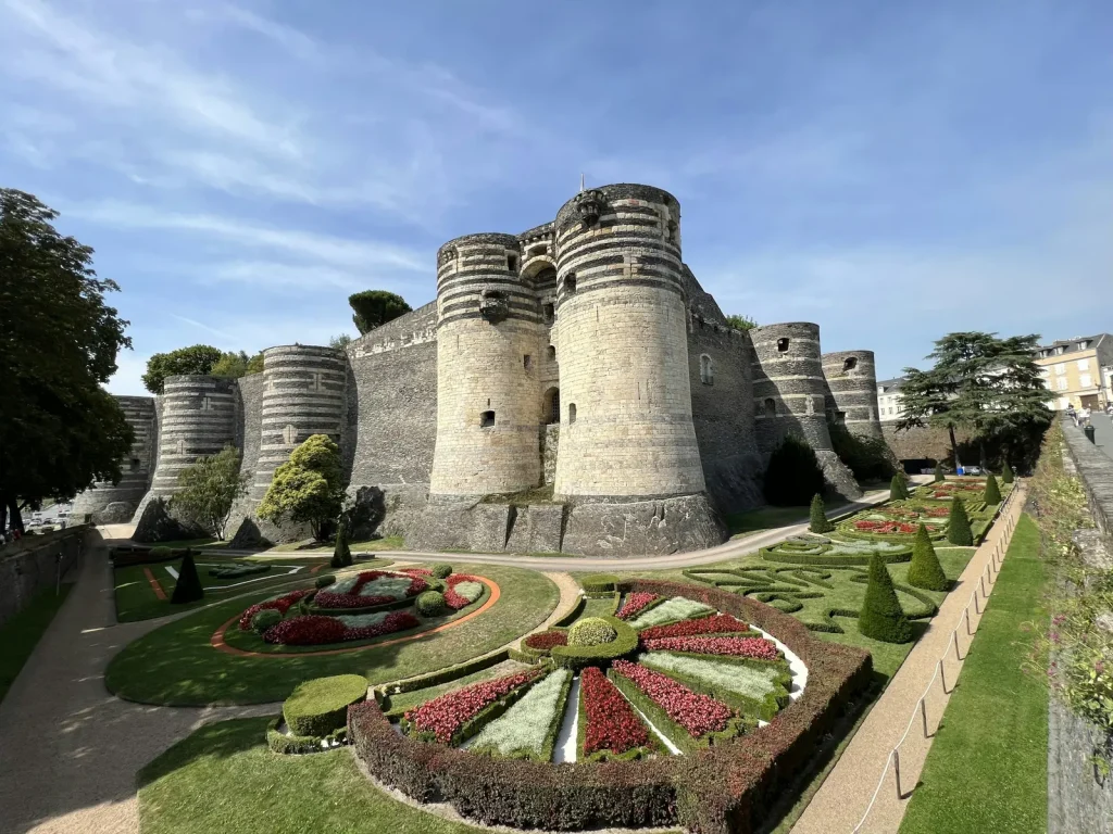 Le château d’Angers, ses tours rayées d’ardoise et ses jardins à la française, sous un ciel bleu
