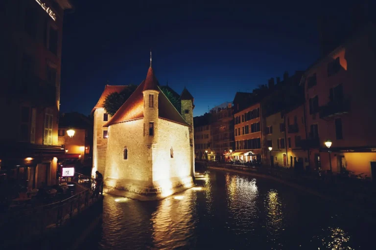 Le Palais de l’Île illuminé sur le Thiou, la nuit, entre les façades de la vieille ville d’Annecy
