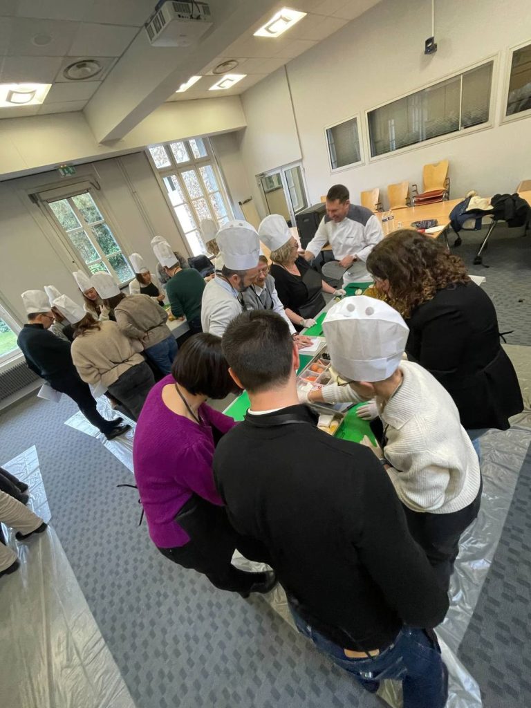 Collaborateurs de Bio-Rad en toques et tabliers, penchés sur les planches à découper pendant le challenge culinaire animé par un chef, dans une salle de leurs locaux de Marnes-la-Coquette