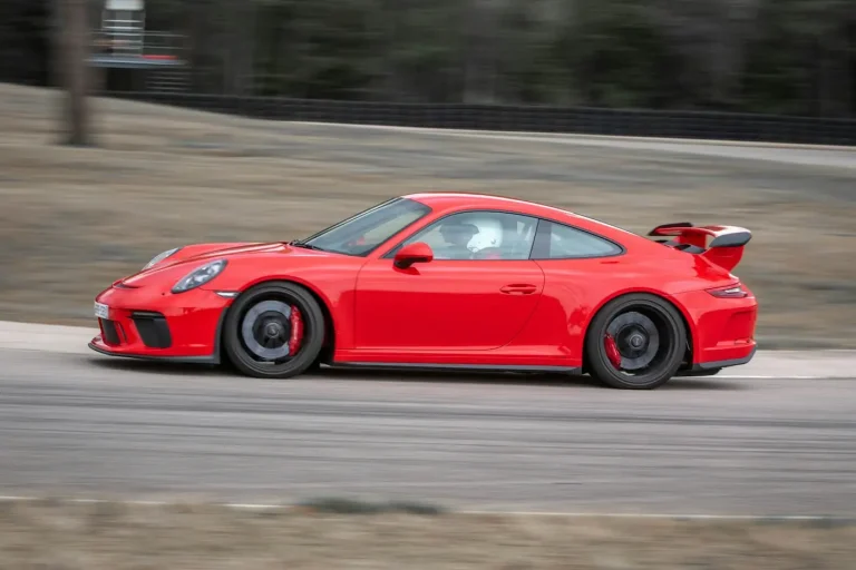 Voiture de sport rouge lancée sur la piste d’un circuit, pilote casqué au volant