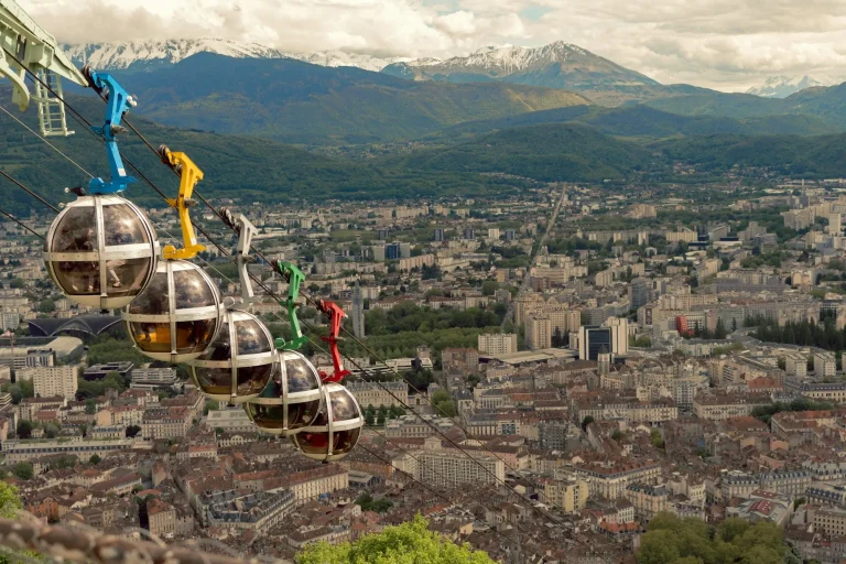 Les « bulles » colorées du téléphérique de la Bastille au-dessus des toits de Grenoble, avec les montagnes à l’horizon