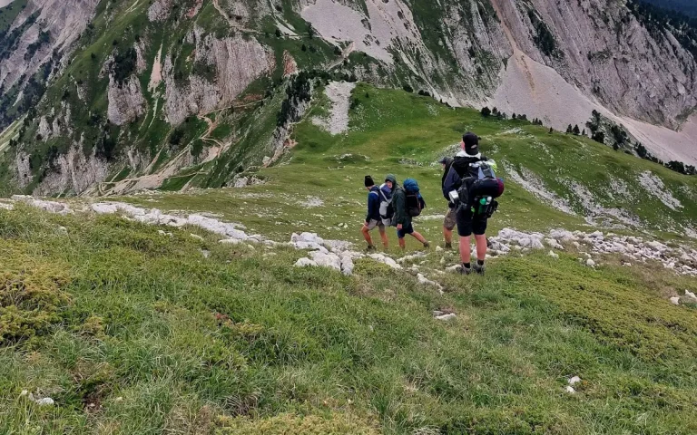 Un groupe de randonneurs, sacs au dos, sur un sentier herbeux au pied des falaises du Vercors