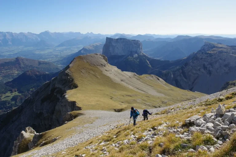 Deux randonneurs sur une crête herbeuse du Vercors, face aux falaises et aux plateaux du massif