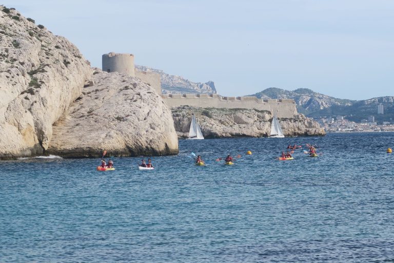 Kayaks du team building de Swiss Life au pied d’un rocher calcaire, au large de Marseille, voiliers en arrière-plan