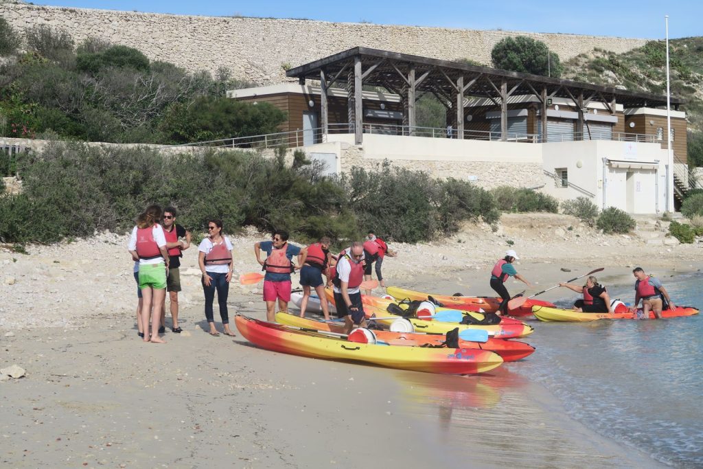Pause sur une plage du Frioul pendant le team building kayak de Swiss Life : participants en gilet de sauvetage et kayaks tirés sur le sable