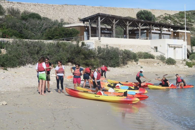 Pause sur une plage du Frioul pendant le team building kayak de Swiss Life, à Marseille : participants en gilet de sauvetage et kayaks tirés sur le sable