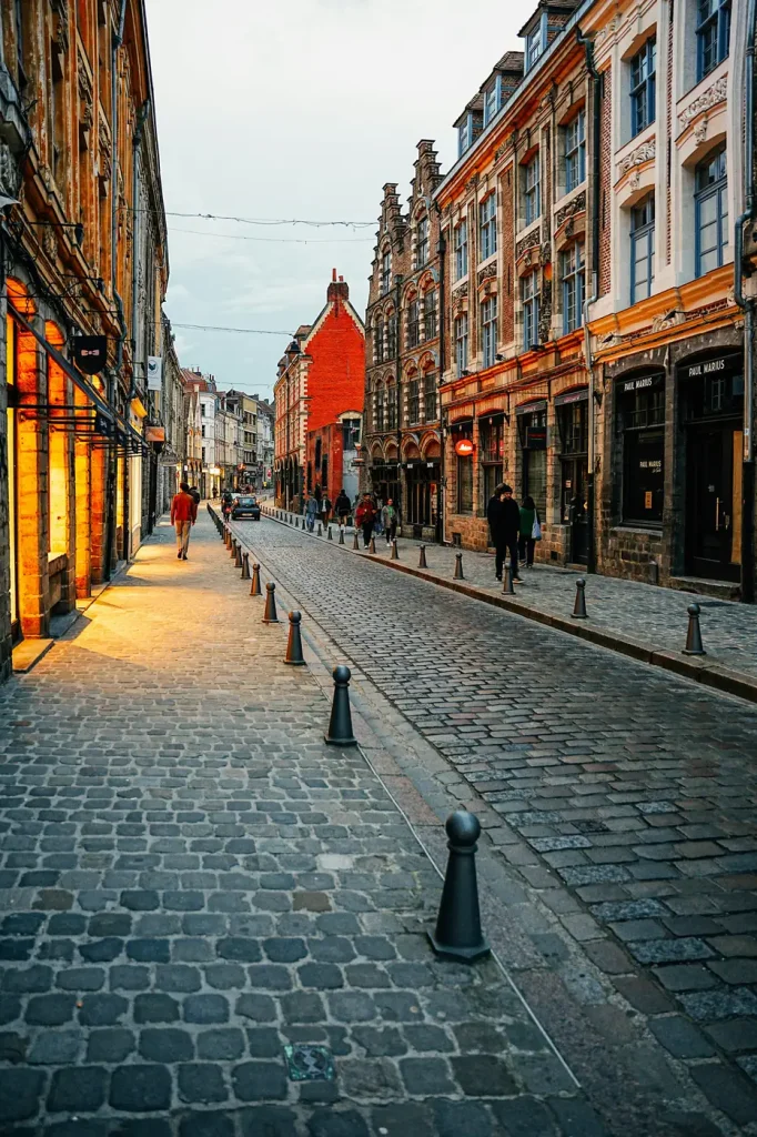 Une rue pavée du Vieux-Lille, bordée de façades anciennes en brique et en pierre, à la tombée du jour