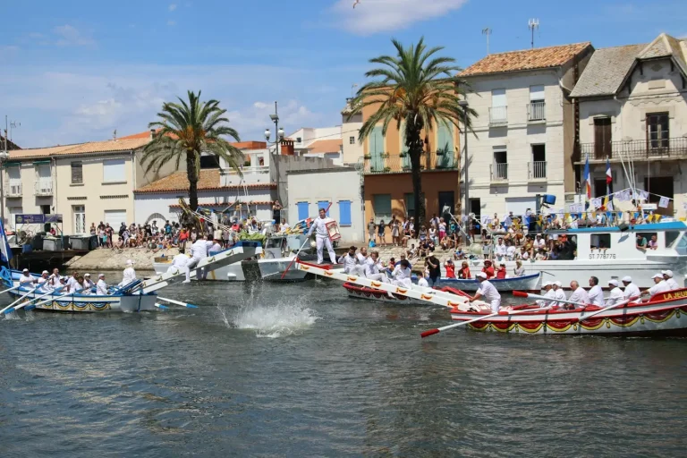 Joute languedocienne dans le chenal du Grau-du-Roi : deux barques à rames se croisent, un jouteur tombe à l’eau sous les yeux du public massé sur le quai