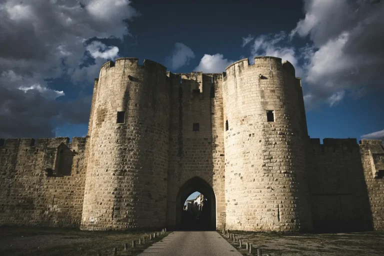 Une porte fortifiée encadrée de deux tours dans les remparts d’Aigues-Mortes, sous un ciel nuageux