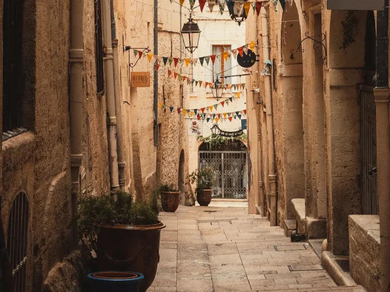 Ruelle dallée du centre historique de Montpellier, entre des façades en pierre blonde, sous des guirlandes de fanions colorés