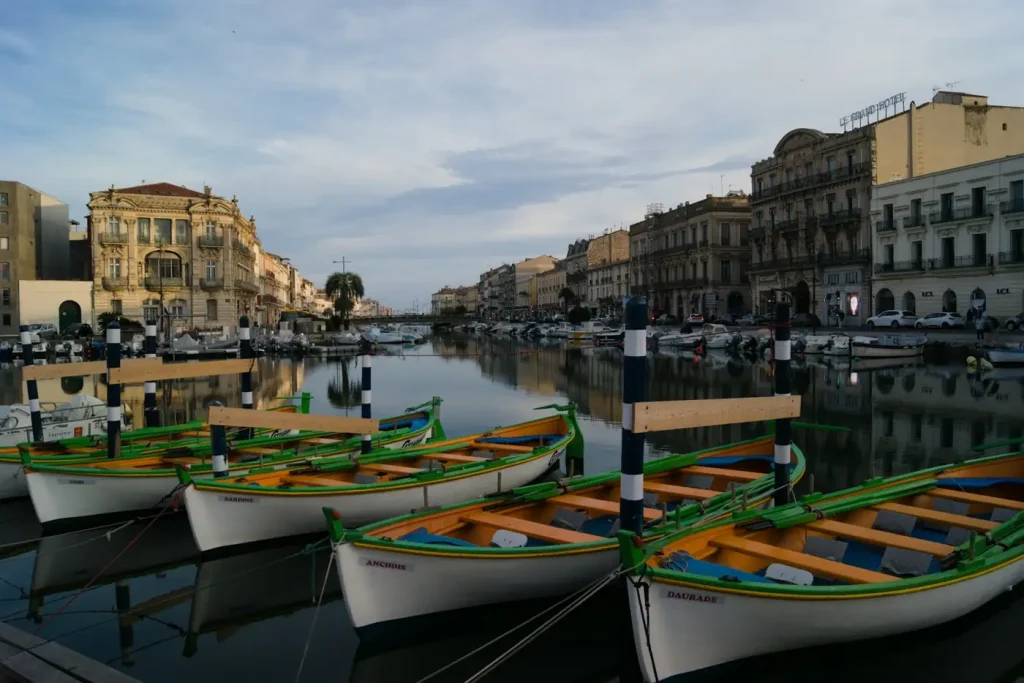 Barques de pêche en bois amarrées le long d’un canal de Sète, devant les façades des quais