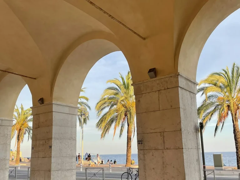 Arcades en pierre ouvertes sur les palmiers et la Méditerranée, au bord du Vieux Nice, dans la lumière du soir