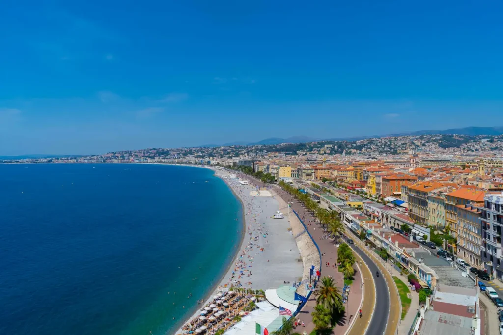 La baie des Anges, sa plage de galets et la Promenade des Anglais qui longe Nice, vues depuis la colline du Château, sous un ciel bleu