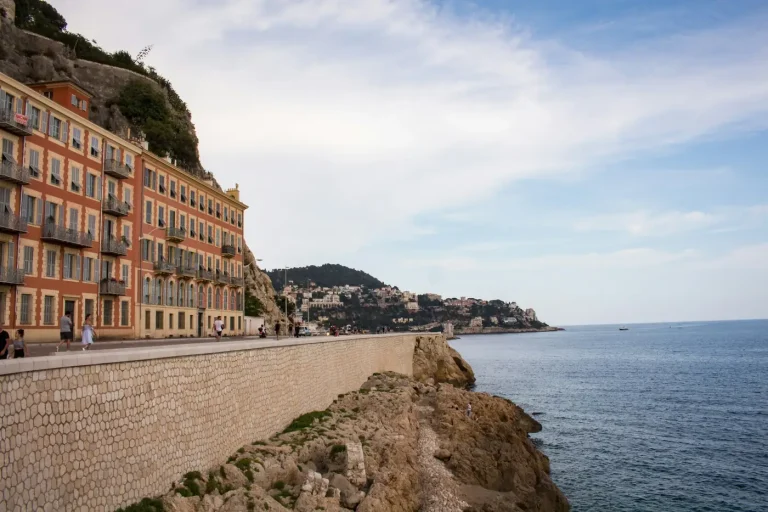 Façades d’immeubles au-dessus d’un mur de pierre et des rochers du bord de mer, côté Cap de Nice, face à la Méditerranée