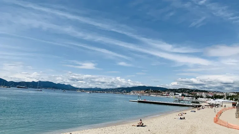 La plage de sable de la pointe Croisette, à Cannes, face à la baie et aux collines, sous un ciel voilé