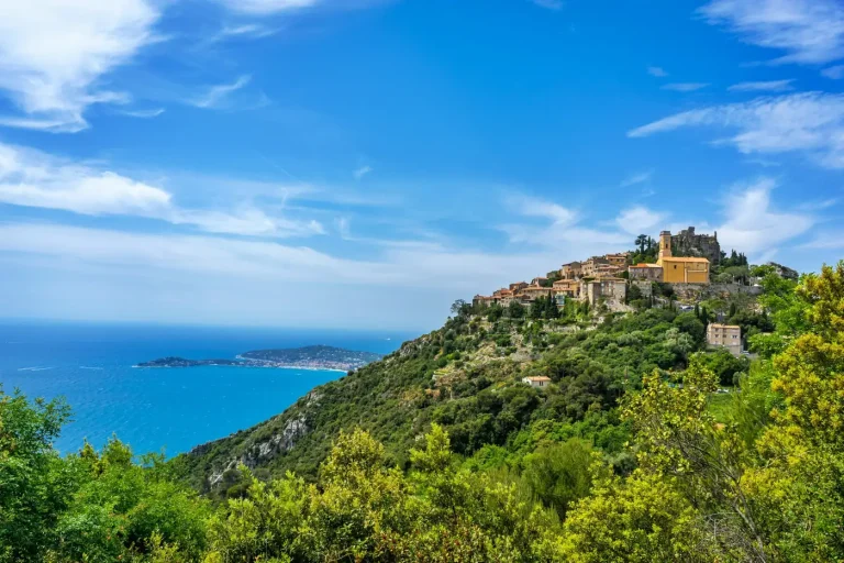 Le village perché d’Èze sur son piton rocheux couvert de pins, au-dessus de la Méditerranée, sous un ciel bleu