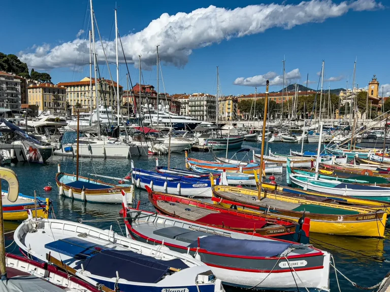 Barques de pêche aux couleurs vives et voiliers amarrés dans le port Lympia, à Nice, sous un ciel bleu et nuageux