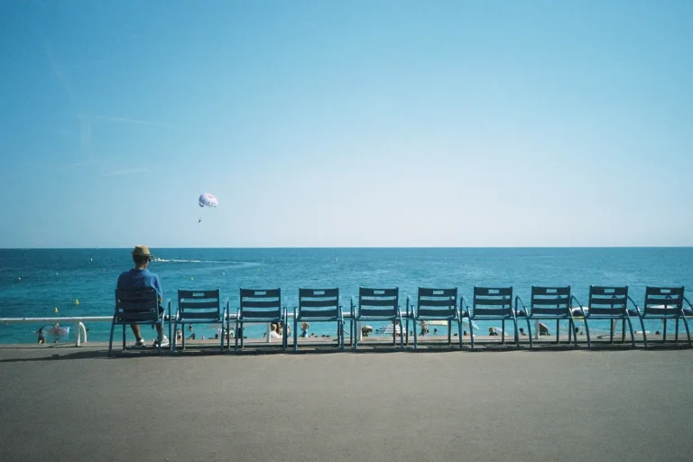 Un promeneur assis au bout d’une rangée de chaises bleues de la Promenade des Anglais, face à la Méditerranée