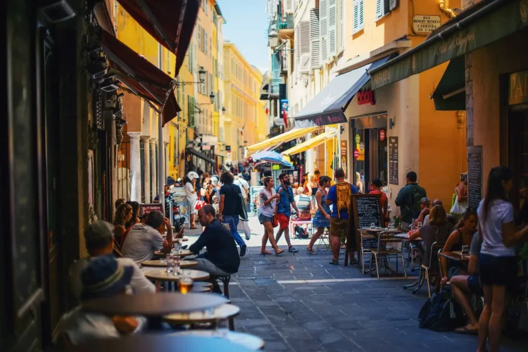 Terrasses de cafés et passants dans la rue Benoît-Bunico, ruelle aux façades ocre et jaunes du Vieux Nice, en plein soleil