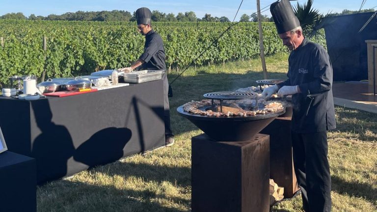 Deux chefs en toque cuisinent au brasero en plein air, face aux vignes, pendant un séminaire au château Lafitte