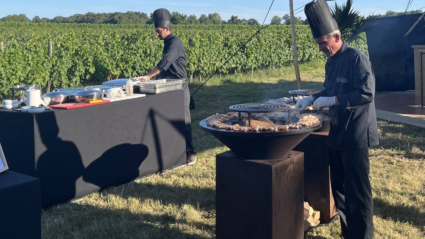 Deux chefs en toque préparent le repas au brasero, en plein air face aux vignes, pendant le séminaire organisé par Weevup au château Lafitte