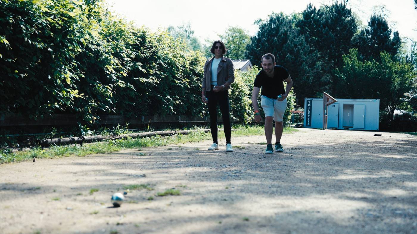 Deux participants du séminaire KPMG lancent leurs boules de pétanque sur une allée de graviers bordée de haies, au Center Parcs du Lac d'Ailette